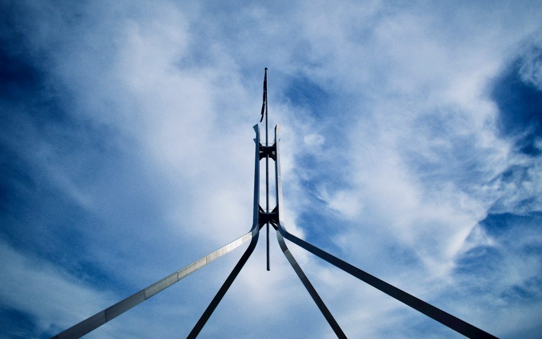 The spire atop parliament house in Canberra Australia against a blue sky with wispy clouds.