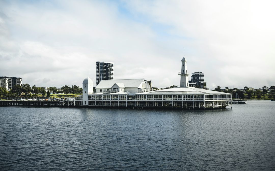 View of the Geelong waterfront and CBD from the sea. A large building is in the foreground overlooking the water. Tall buildings are visible in the background.