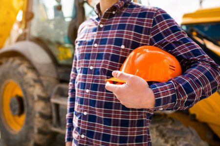 Construction worker holding a helmet, heavy machinery in the background.